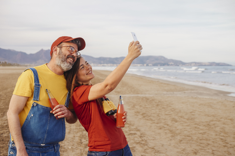 Paar mit alkoholfreien Getränken macht Selfie mit Smartphone am Strand, lizenzfreies Stockfoto