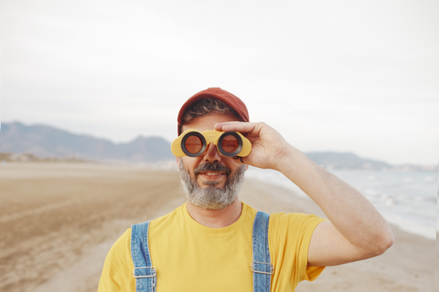 Bearded man using binoculars on the beach stock photo