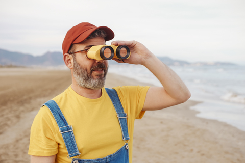 Bärtiger Mann mit Fernglas am Strand, lizenzfreies Stockfoto