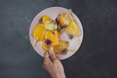 Hand taking homemade orange lemon popsicle with edible flowers from plate - SKCF00440