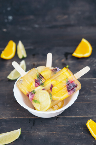 Bowl of homemade orange and lemon popsicles with edible flowers stock photo