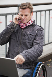 Mann im Rollstuhl, der mit einem Laptop auf dem Schoß telefoniert - MASF06761