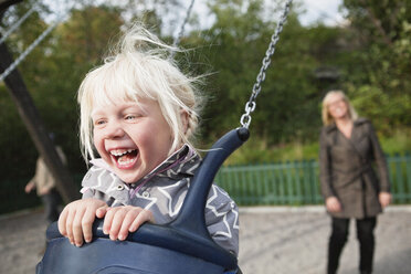 Daughter (2-3) in swing with mother in the background - MASF06770