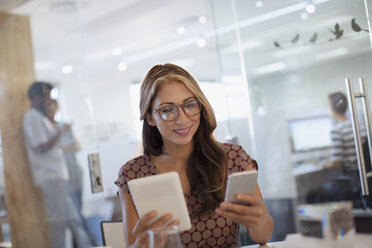 Geschäftsfrau beim Multitasking, mit Smartphone und digitalem Tablet im Büro - HOXF03405