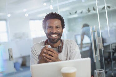 Portrait smiling, confident creative businessman using smart phone at laptop in office - HOXF03415