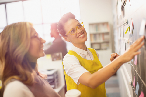 Lächelnde, selbstbewusste, kreative Geschäftsfrauen, die an der Tafel planen und Brainstorming betreiben, lizenzfreies Stockfoto