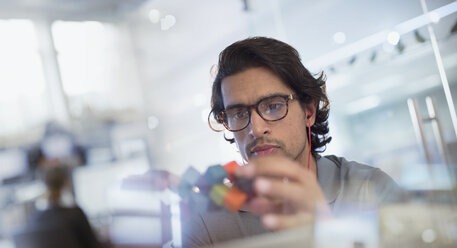 Focused, innovative male entrepreneur examining prototype in office - HOXF03444