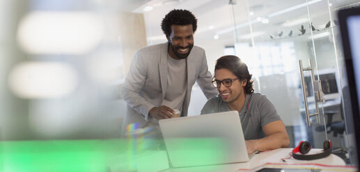 Lächelnde kreative Geschäftsleute arbeiten am Laptop im Büro - HOXF03452