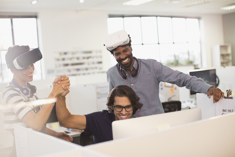 Lächelnde, begeisterte Computerprogrammierer, die sich die Hände reichen und Virtual-Reality-Simulatorbrillen testen, lizenzfreies Stockfoto