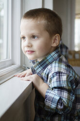 Lächelnder Junge schaut durch das Fenster, während er zu Hause steht - CAVF45733