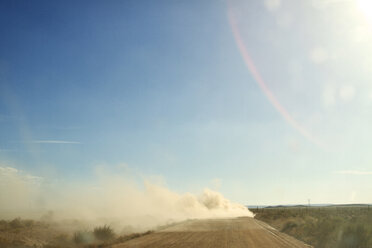 Dust on dirt road amidst field against blue sky during sunny day stock photo