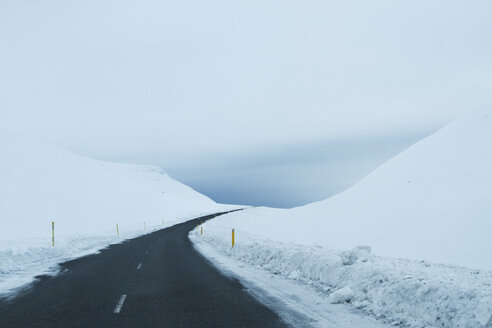 Leere Landstraße inmitten eines verschneiten Feldes vor bewölktem Himmel - CAVF45842