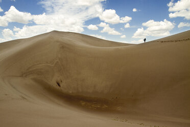 Distant view of hiker walking on sand in desert against sky - CAVF45872