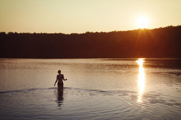 Rückansicht einer Frau im Bikini, die bei Sonnenuntergang im See steht - CAVF45881