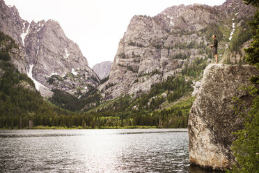 Low angle view of man with stick standing on rock amidst lake - CAVF45907