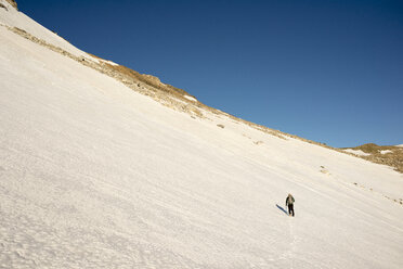 Rückansicht eines Mannes, der auf einem verschneiten Feld gegen einen klaren blauen Himmel wandert - CAVF45912