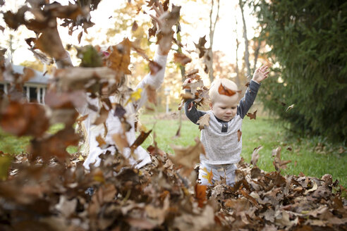 Fröhliche Geschwister spielen mit trockenen Blättern im Hinterhof - CAVF45954