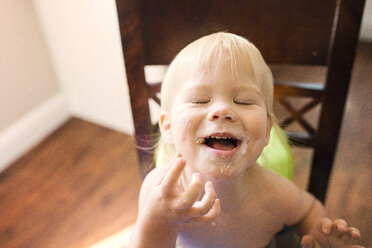 High angle view of happy boy with messy mouth sitting on chair - CAVF45964
