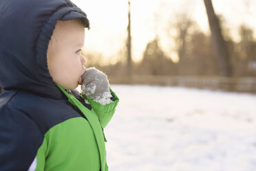 Junge mit Finger im Mund schaut weg, während er im Winter im Hinterhof steht - CAVF45973