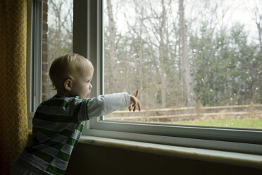 Junge schaut durch das Fenster, während er zu Hause steht - CAVF45976