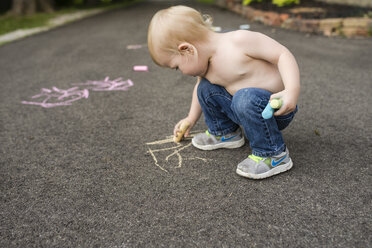 Shirtless boy writing with chalk on footpath - CAVF45979
