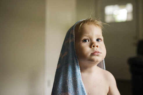 Junge mit Handtuch auf dem Kopf schaut weg, während er zu Hause sitzt - CAVF45984