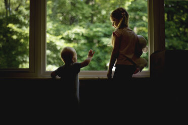 Mädchen sieht ihren Bruder am Fenster stehend an - CAVF45993