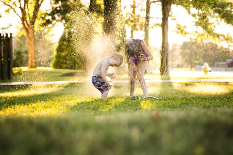Fröhliche Geschwister, die im Hinterhof mit Wasser spielen, lizenzfreies Stockfoto
