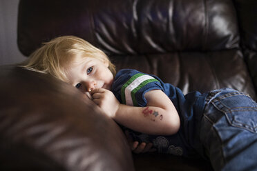 Niedlicher Junge schaut weg, während er sich zu Hause auf dem Sofa entspannt - CAVF46018