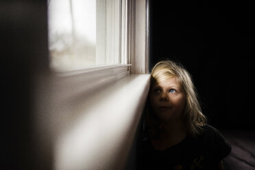 Thoughtful girl looking through window while sitting at home - CAVF46048