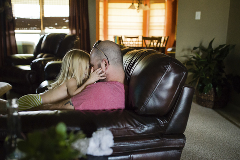 Vater spielt mit seiner Tochter ohne Hemd, während er zu Hause auf dem Sofa sitzt, lizenzfreies Stockfoto