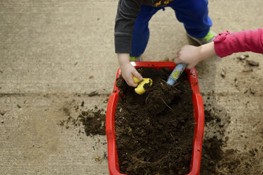 Ausgeschnittenes Bild von Geschwistern, die im Garten mit Schlamm spielen - CAVF46065