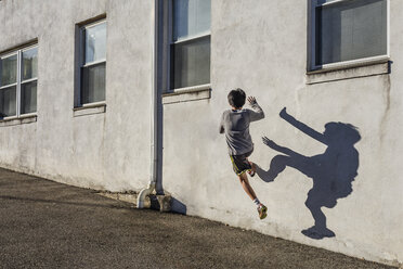 Rear view of teenage boy jumping over wall during sunny day - CAVF46073