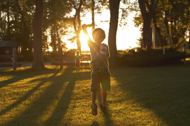 Siblings playing on grassy field in park during sunset - CAVF46092