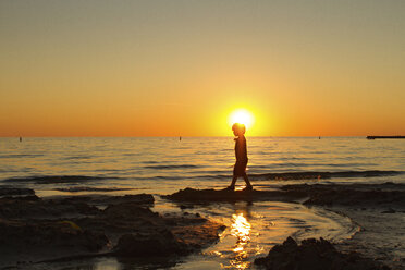 Side view of silhouette boy walking at beach during sunset - CAVF46094