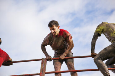 Low angle view of man climbing obstacle against cloudy sky during race - CAVF46141