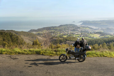 Älteres Paar mit Blick auf die Berge, während es mit dem Motorrad auf der Straße steht - CAVF46143