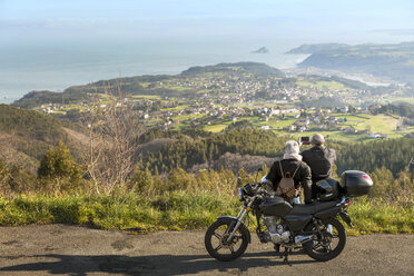 Älteres Paar fotografiert Berge, während es auf der Straße neben einem Motorrad steht - CAVF46144