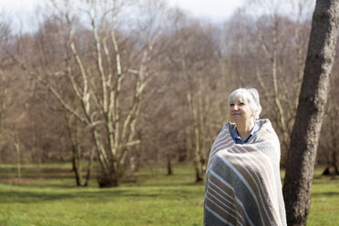 Thoughtful senior woman wrapped in blanket standing on field during winter - CAVF46147