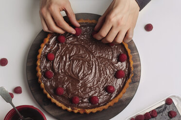 Mann dekoriert Schokoladenkuchen mit Himbeeren - CAVF46156