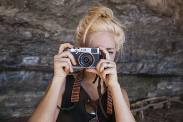 Young woman photographing through vintage camera against rock - CAVF46198
