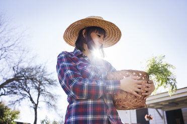 Junge Bäuerin trägt Korb auf einem Bauernhof an einem sonnigen Tag - CAVF46200