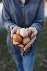 Midsection of farmer holding eggs while standing on lakeshore - CAVF46218