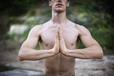 Mittelteil eines hemdlosen Mannes mit verschränkten Händen, der im Freien Yoga praktiziert - CAVF46222