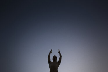 Low angle view of shirtless man standing with arms raised while meditating against sky at night - CAVF46225