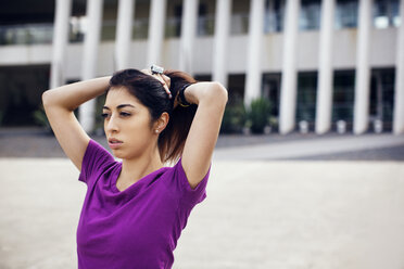 Thoughtful female athlete tying ponytail on footpath - CAVF46227