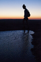 Silhouette einer Frau, die während des Sonnenuntergangs an einem Teich auf einem Feld spazieren geht - CAVF46243