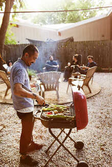 Mann beim Grillen, während Freunde im Hof sitzen - CAVF46282