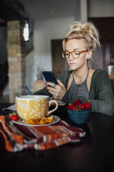 Frau, die am Frühstückstisch sitzend ihr Smartphone benutzt - CAVF46338