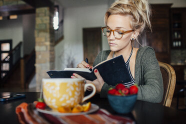 Woman writing diary while sitting at breakfast table - CAVF46339